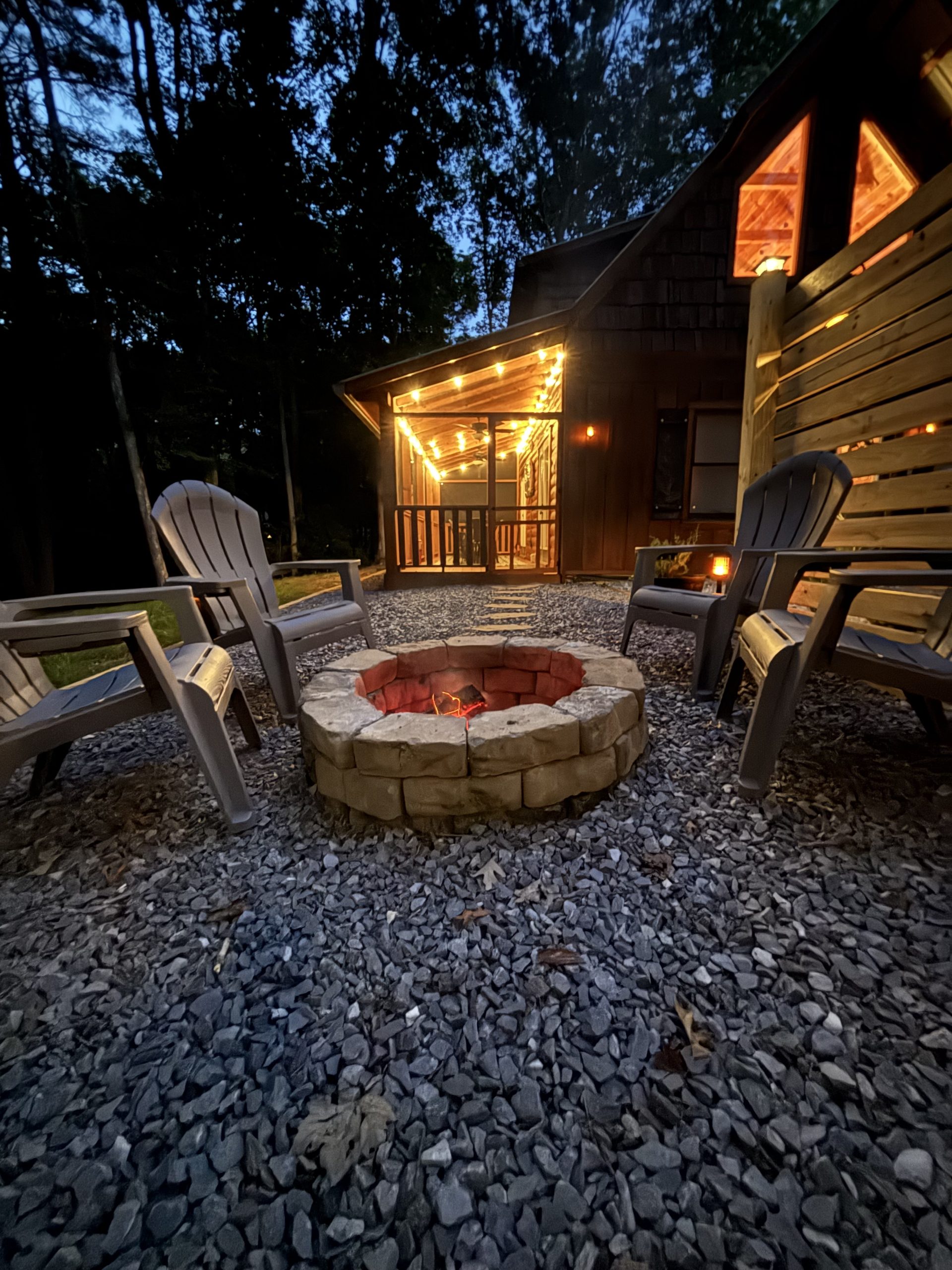 Private fire pit at dusk with Adirondack seating and the illuminated screened porch at The Cozy Nook