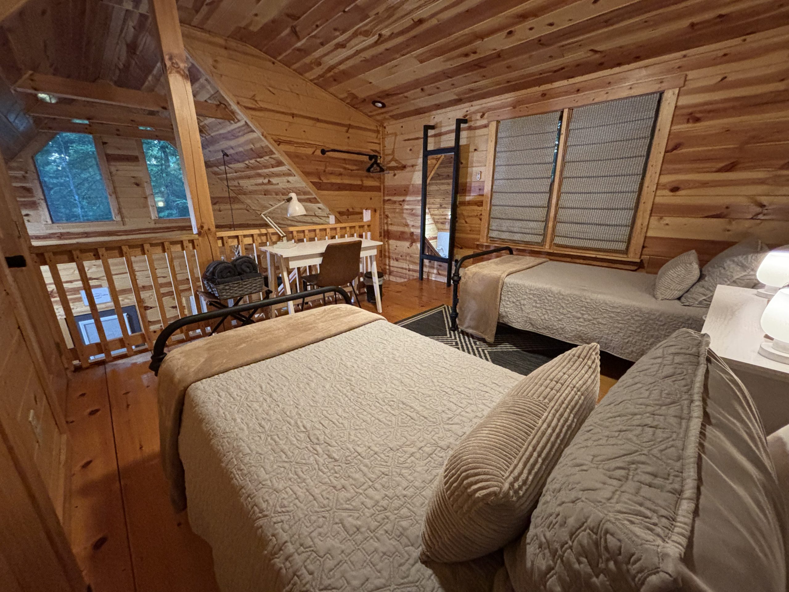 Wide alternate view of the loft with two twin beds, workspace, railing and windows at The Cozy Nook